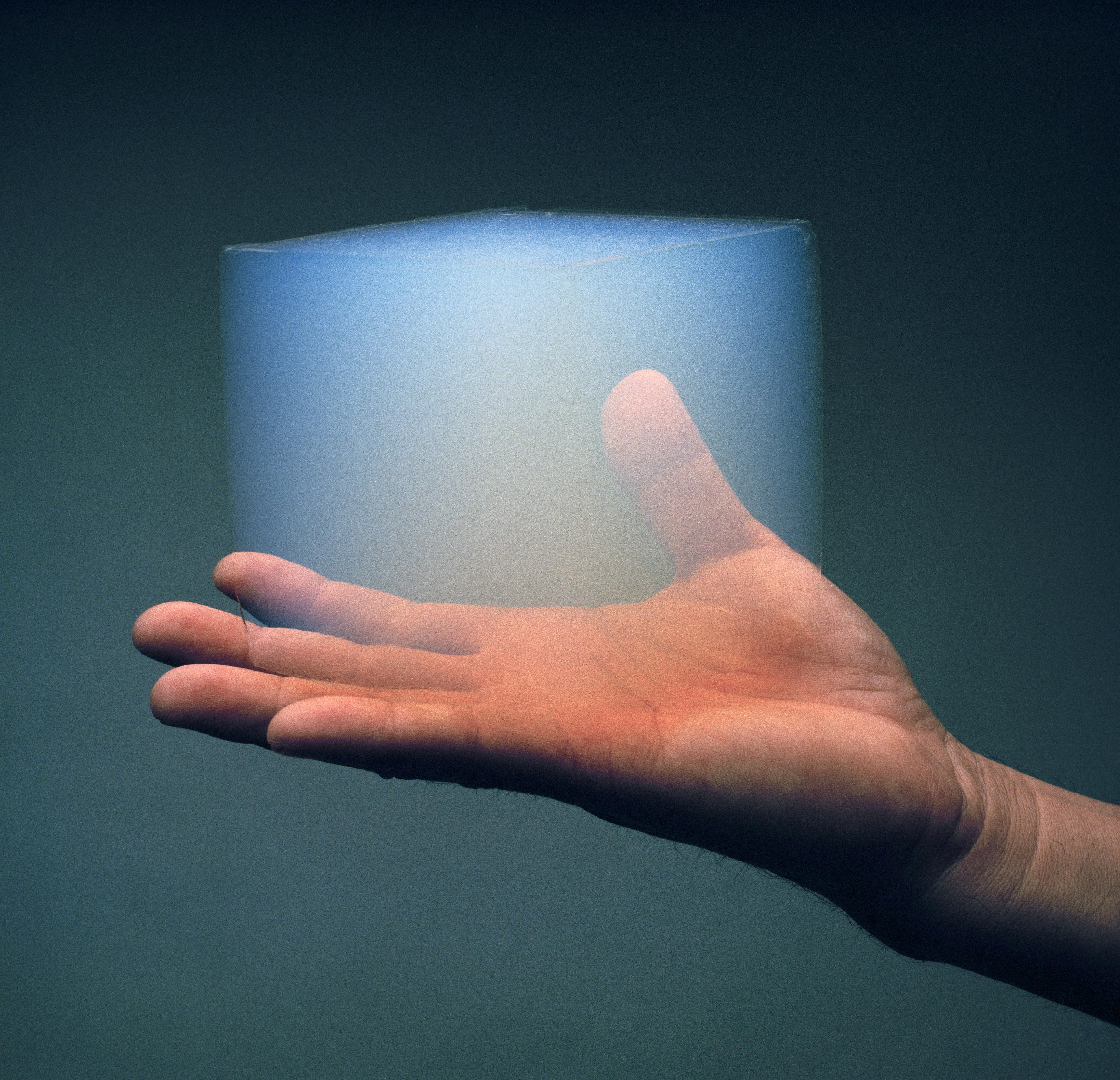 Eine Hand hält einen transparenten Aerogelblock.
